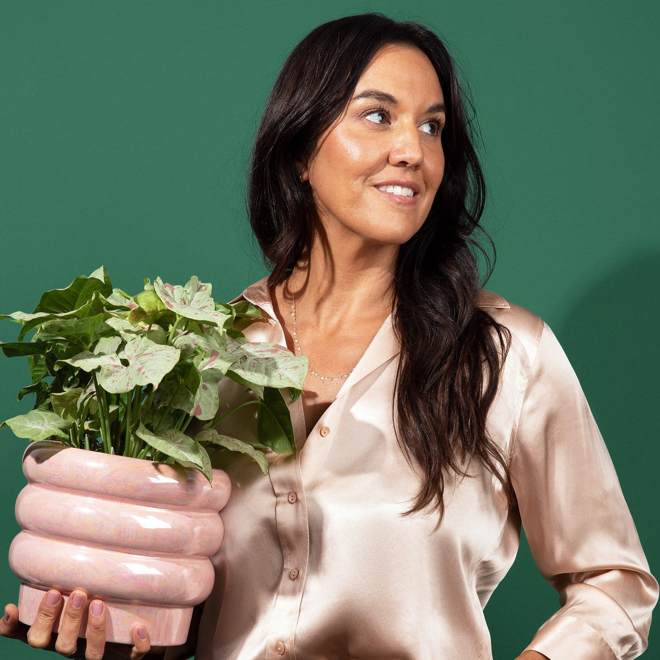 Emily from Southside holding a pink ceramic pot with green plant against a green background